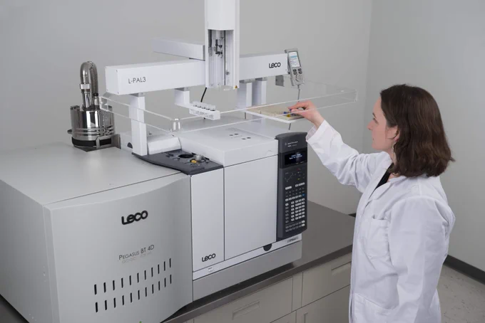 Scientist operating a LECO Pegasus 4D gas chromatograph in a laboratory setting.
