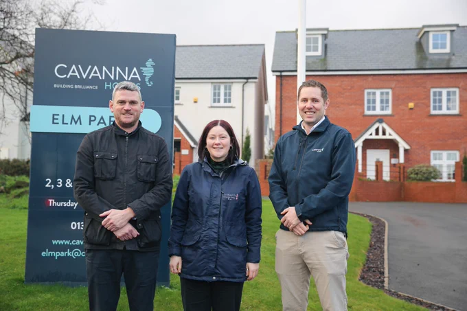 Three people standing in front of a sign and some new homes.