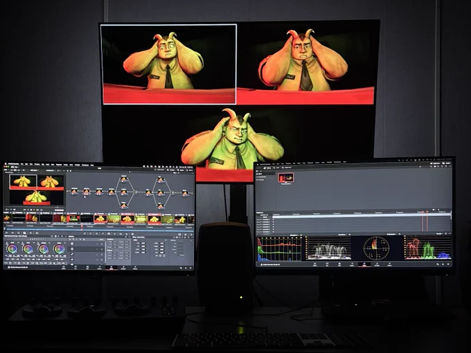 Multiple computer monitors display a video editing and color grading workspace featuring scenes from an animated film. The main screen shows a character in three different shots, while the lower monitors display editing software with color and waveform charts.