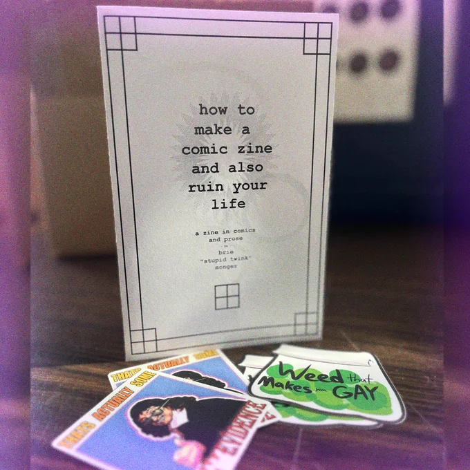 white zine with black text that says: "how to make a comic zine and also ruin your life - a zine in comics and prose - brie "stupid twink" monger". there a is also a set of stickers below it