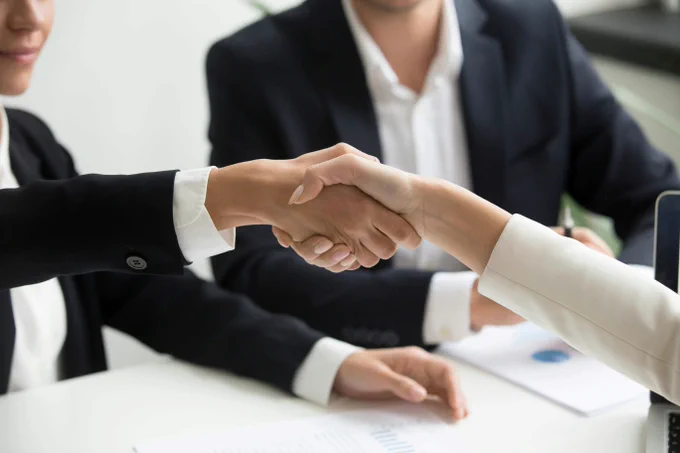 Close up of people shaking hands. The people are wearing suits and sitting at a table.