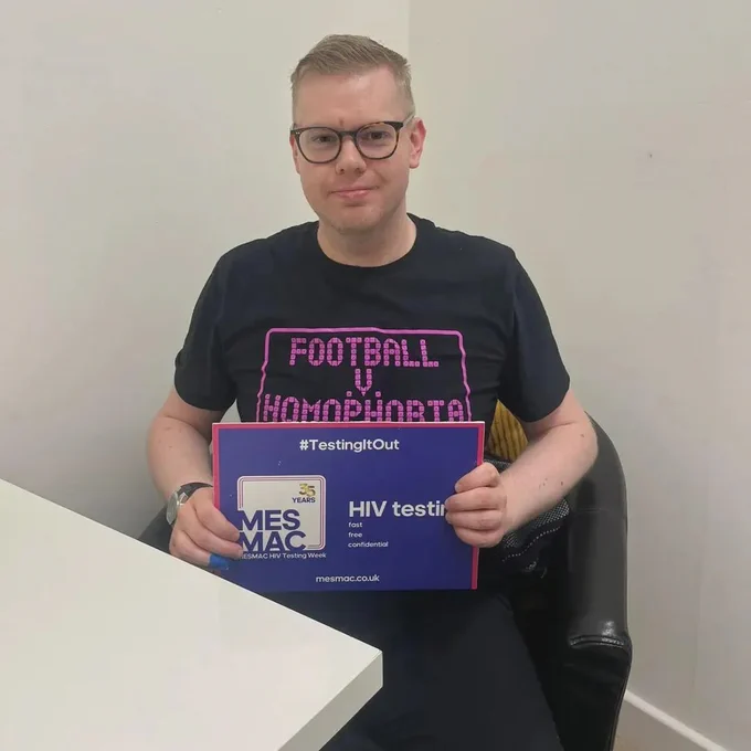 A photo of me holding a HIV Testing Week sign while wearing a Football v Homophobia T-shirt.