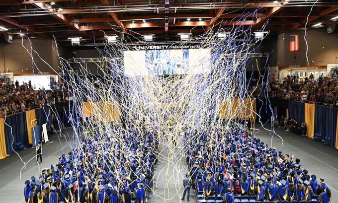 Graduates standing at Commencement as confetti rains down.