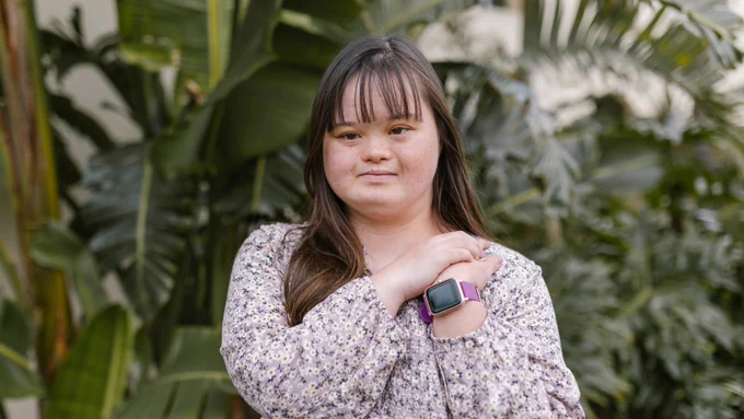 White text in a blue box reads "People with intellectual and developmental disabilities deserve access to healthcare." To the left is a photo of a young white woman wearing a yellow cardigan, smiling and looking at someone off camera.
