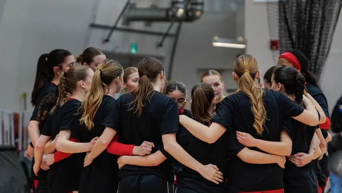 A basketball team wearing matching black shirts with red accents inside a gym.