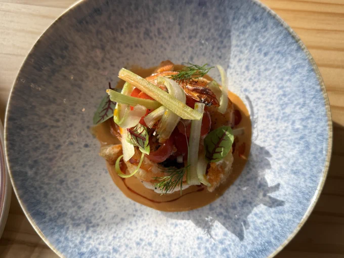 Gourmet dish with layered vegetables and herbs on a creamy sauce in a textured blue bowl.
