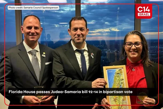 Three people stand smiling, dressed in formal attire. One holds a framed map of Israel. The background shows a cityscape at sunset.