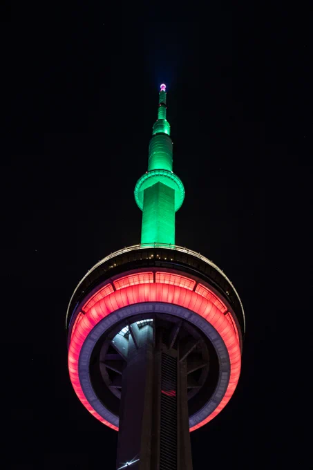 Closeup of the CN Tower at night lit red, black and green / Gros plan de la Tour CN illuminée en rouge, noir et vert la nuit.