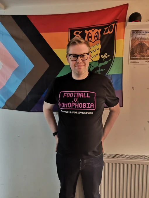 A photo of Rainbow Owls founder and chair Chris Ledger wearing a Football v Homophobia T-shirt in front of the SWFC Progress Pride banner.