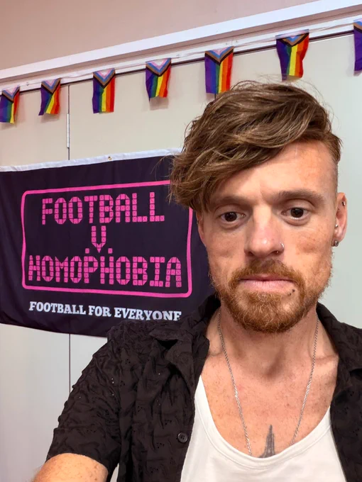 A photo of Rainbow Owls campaigns officer Sam-Elliott Olechnowicz in front of the Football v Homophobia banner.