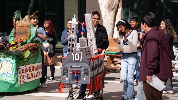 Students smiling and admiring their own creation of a Spider-Man/TAMIU themed shopping cart.
