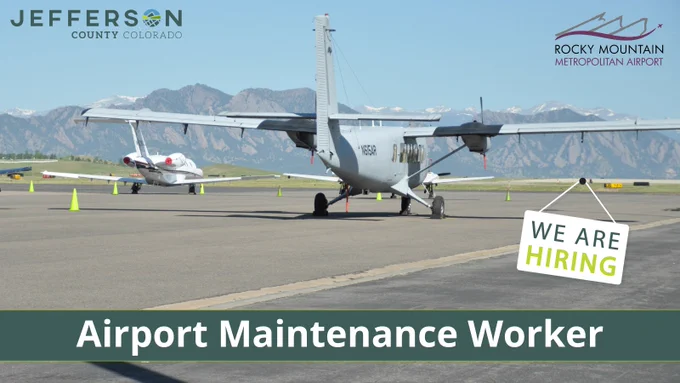 An airplane is parked on a tarmac at Rocky Mountain Metropolitan Airport. Another small plane is visible in the background. 

A sign reads, "We Are Hiring - Airport Maintenance Worker."