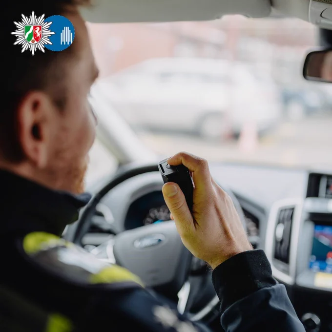 Symbolfoto. Ein Polizist am Steuer des Streifenwagens hält das Funkgerät in der rechten Hand