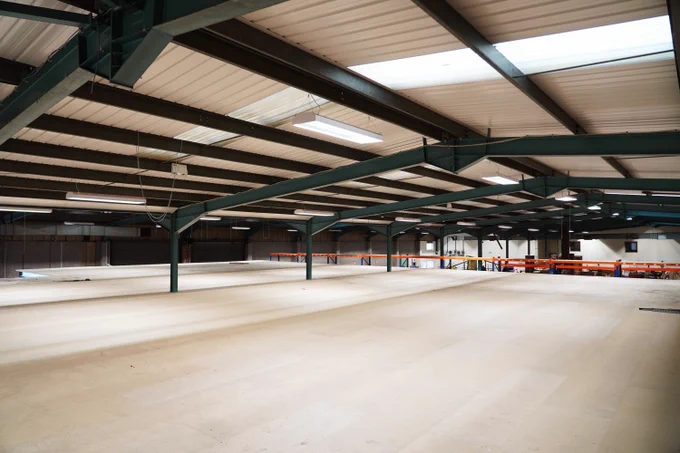A large warehouse space with steel girders and wooden flooring is empty.