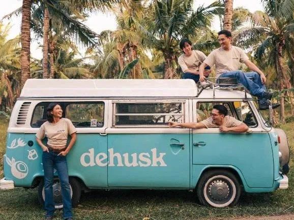 Four people pose on top of a 1970s campervan branded as Dehusk.