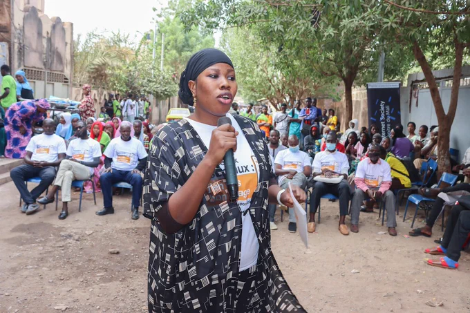 A woman stands and speaks into a microphone at a Mali Chapter event