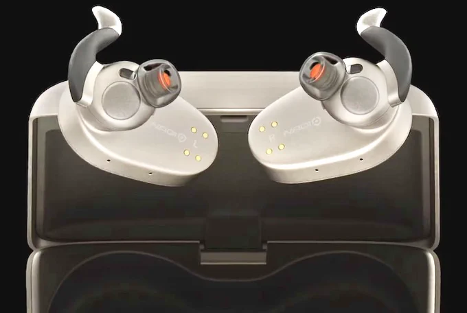 Close-up view of a pair of NaqiLogix neural earbuds. They are black and silver in color and futuristic in appearance as they rest in an open black charging case. Each earbud has a curved black ear hook, a cylindrical black bud with a red interior, and four small gold contact pins on the outer surface, set against a dark background.
