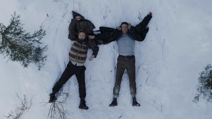 A first look at Mayday, starring Ryan Reynolds and Kenneth Branagh. The two are lying in the snow with their arms sprawled out, looking disheveled.