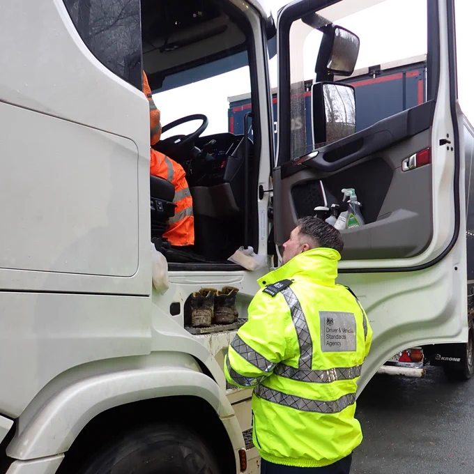 A DVSA officer is talking to a lorry driver who is sat in the lorry cab.