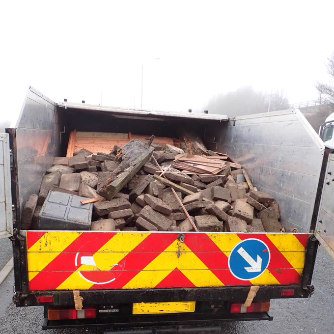 A van with an open top back is shown with a load of construction waste. 