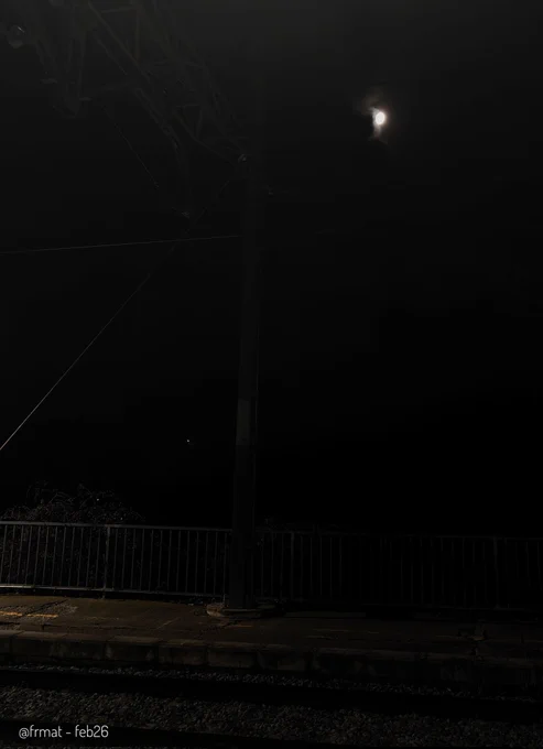Lluna plena sobre la catenària a les fosques i un petit tros d'andana i de via il·luminat per un fanal de l'estació. 