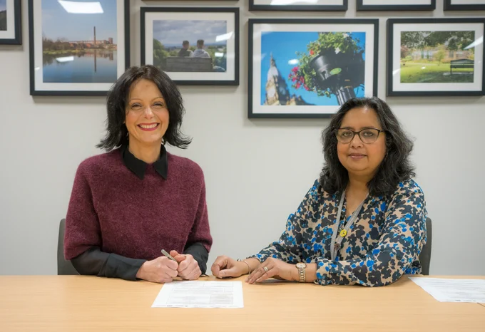 A picture of Group Chief Executive, Caroline Simpson signing a pledge. She is sat next to the Director of People Services, Mallicka Mandal. Both are smiling.