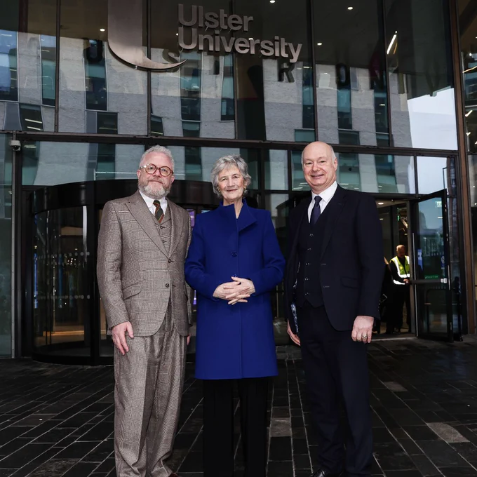 Ulster University Chancellor Dr. Colin Davidson alongside President of Ireland Catherine Connolly and Vice-Chancellor Paul Bartholomew standing outside the glass entrance of Ulster University's Mary Ann McCracken Building.