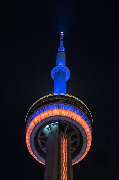 Closeup of the CN Tower at night lit orange and blue / Gros plan de la Tour CN illuminée en orange et bleu la nuit.  
