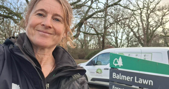New Forest NPA ranger takes a selfie in front of a National Park car park sign and a NPA van branded with the New Forest code