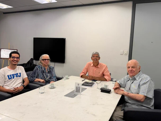 Fotografia de quatro pessoas sentadas ao redor de uma mesa retangular clara, durante reunião sobre pedido de diplomação póstuma de estudantes mortos pela ditadura. Entre elas estão: Lucas Duda, representante do Centro Acadêmico Stuart Angel (Casa), do Instituto de Economia (IE) da UFRJ;  a jornalista Hildegard Angel e o reitor da UFRJ, Roberto Medronho.