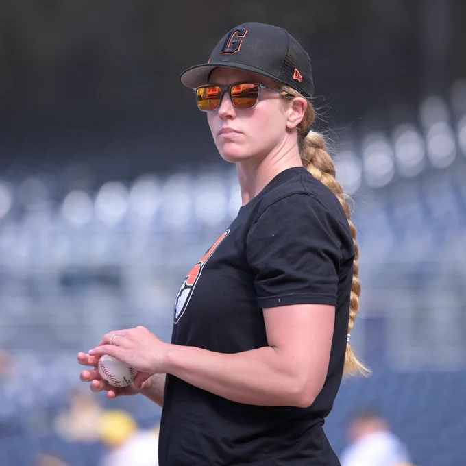 Alyssa Nakken looks forward while holding a baseball and wearing a black t shirt and sunglasses