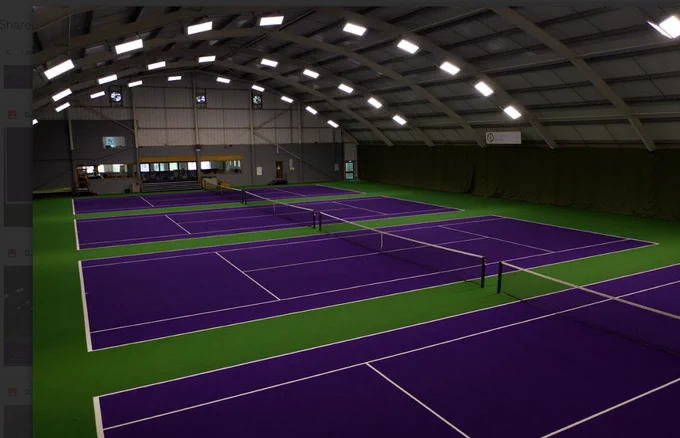 Indoor tennis facility with multiple purple courts and green borders under bright overhead lights.
