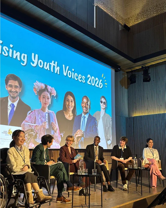 6 panelists sit on stage and look at one another smiling.