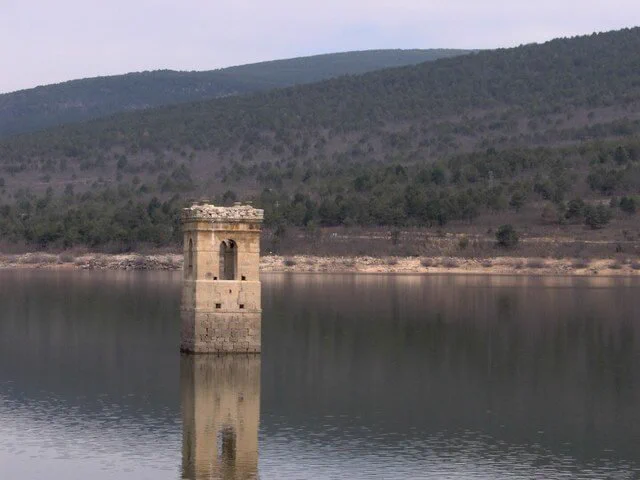 Un pantano lleno de agua, en mitad del cual emerge la torre de una iglesia, de la que solo vemos el campanario sobresaliendo del agua.