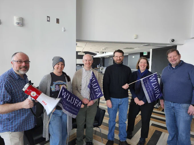 Six WLUFA Members posing for a photo with WLUFA flags and a bullhorn. 