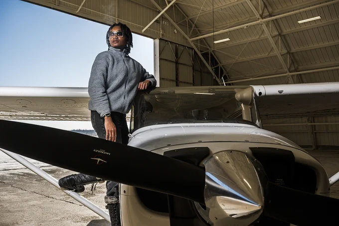  Ashanti Mallit stands confidently next to an aircraft's propeller in an open hangar.
