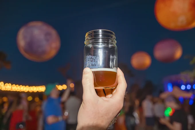 someone holding a beer glass with crowd in back