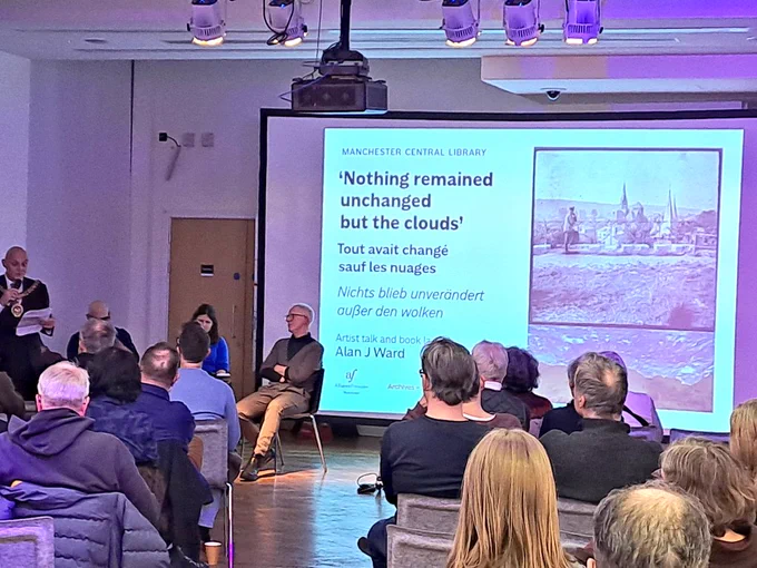 Man speaking to audience in front of illuminated historic photos 