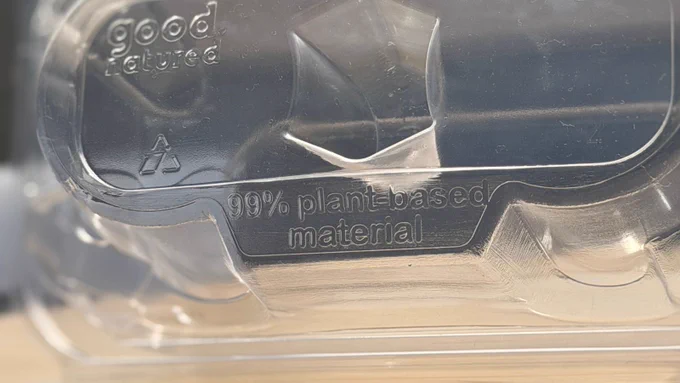 Macro shot of the container bottom embossed with "good natured" logo and "99% plant-based material" text, confirming BPI-certified compostable PLA.