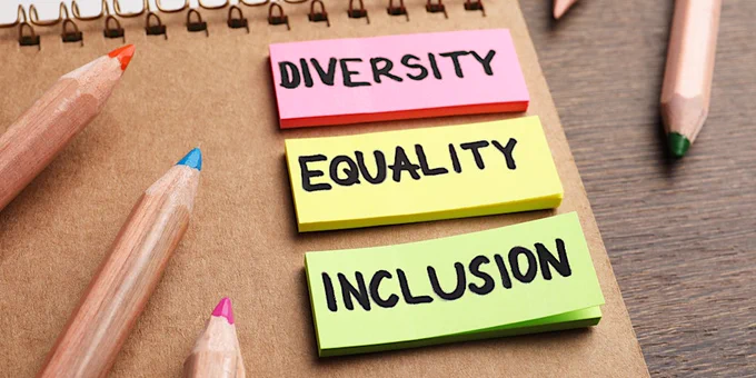 Three colorful sticky notes labeled Diversity, Equality, and Inclusion on a brown notebook with colored pencils nearby.
