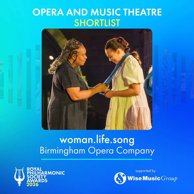 This image shows two people sharing a moment, standing close to each other. Text on the image states that an opera called "woman.life.song," by the Birmingham Opera Company has been shortlisted for the Royal Philharmonic Society Award for Opera and Music Theatre award. The background is a gradient of blue colours.