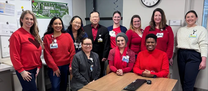A group of eleven healthcare workers are posing indoors. Most are wearing red tops. Visible text includes, \"STOP THE@1 KNOW@2 HEALTH@3 YOU@4 ARE@5 EXIT@6\"