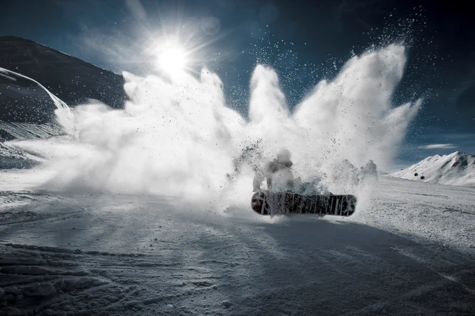 Snowboarder carving sharply through fresh powder, sending a dramatic spray of snow into the bright mountain air.