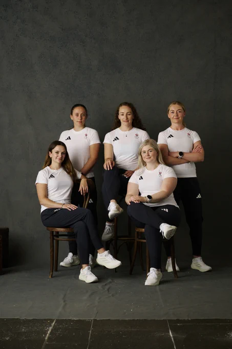 Five athletes in matching white Adidas shirts and black pants posing against a dark gray backdrop, three seated and two standing.