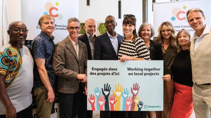 A photo of Emily Jones Joanisse and other members of the Connected Canadians team smiling and posing behind a sign from Desjardins that says “Engagés dans des projets d'ici / Working together on local projects.” 