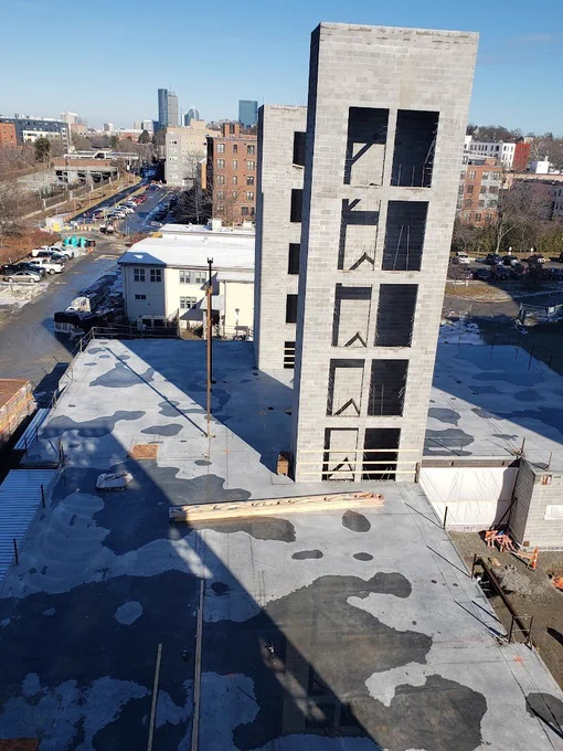 A photo of two tall concrete structures being built at the Amory Street development with multiple window openings on a flat rooftop in an urban area under a clear blue sky.