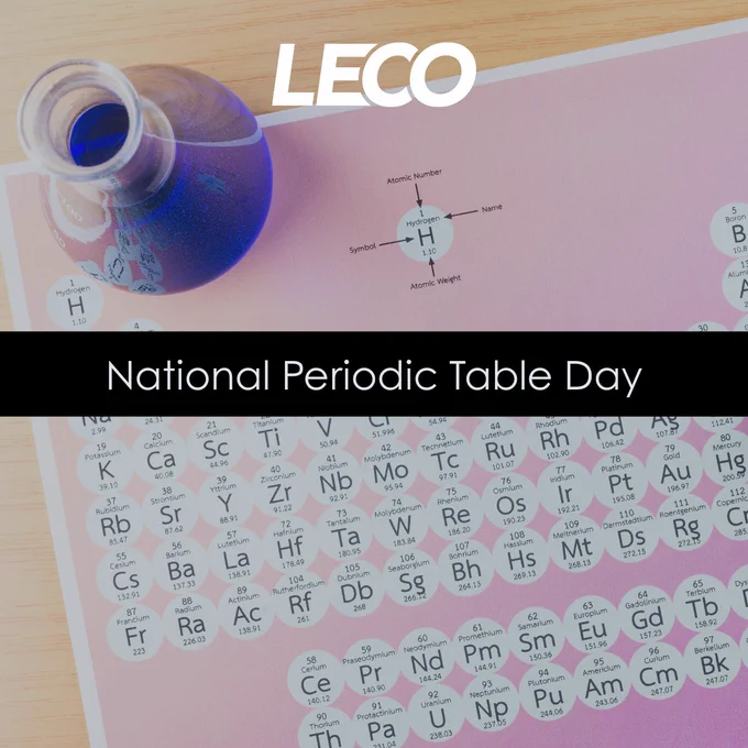 Close-up of a periodic table page with a blue liquid-filled flask, highlighting the element Hydrogen and celebrating National Periodic Table Day.