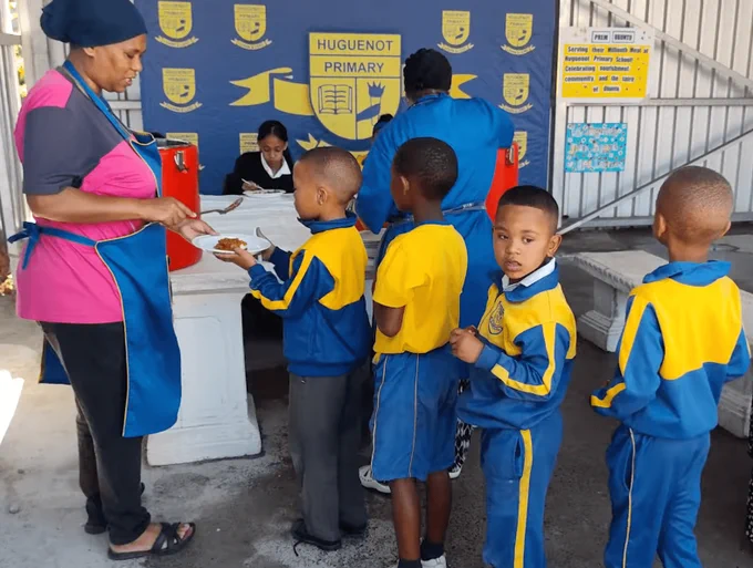 Young school children line up for a nutritious meal served by a staff member of TPRF's Food for People facility in Cape Flats, South Africa