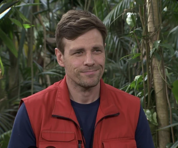 Clemens Fritz in einer roten Weste und dunklem T-Shirt mit Dschungel im Hintergrund.