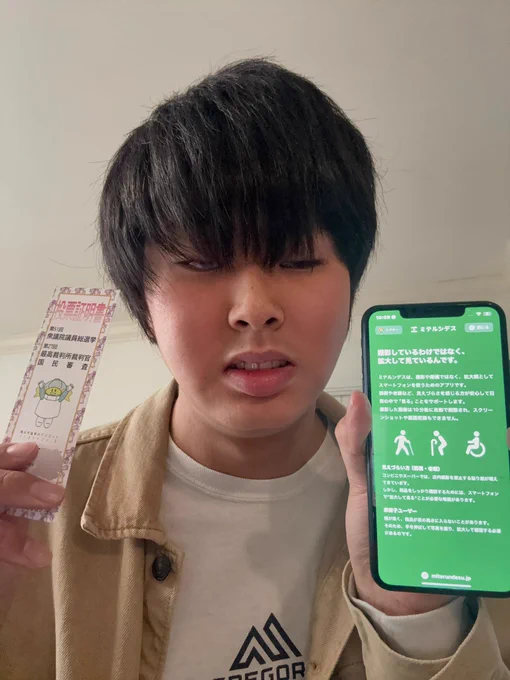 左手に投票証明書、右手に拡大したいるわけではなくミテルンデスという説明画面を表示したスマートフォンを持つ投稿主。